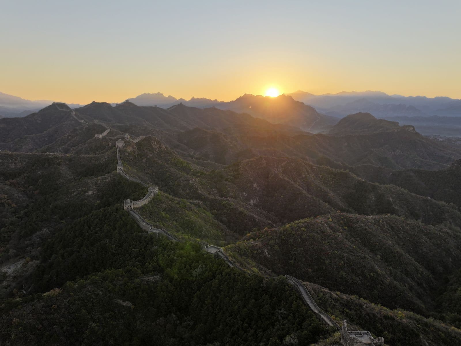 Sunrise over the Great Wall winding through green mountains